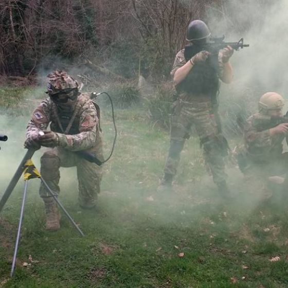 Four people in tactical gear with rifles in a smoky outdoor setting.